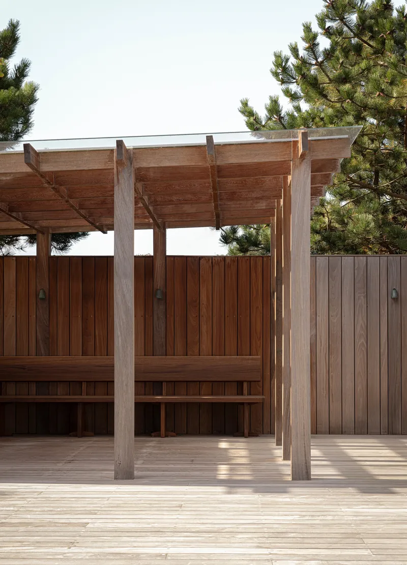 Timber pergola with exposed rafters and columns over a deck with vertical wood fence