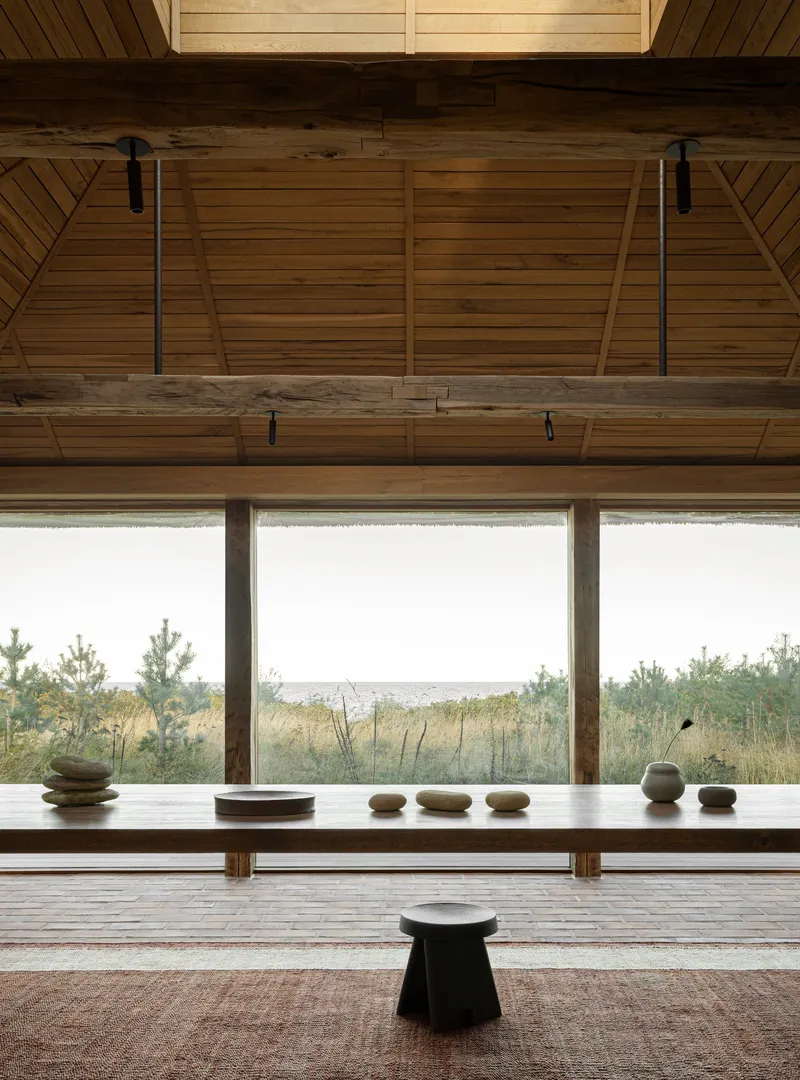 Interior view with timber bench, stone objects and full-width windows framing the distant coastline