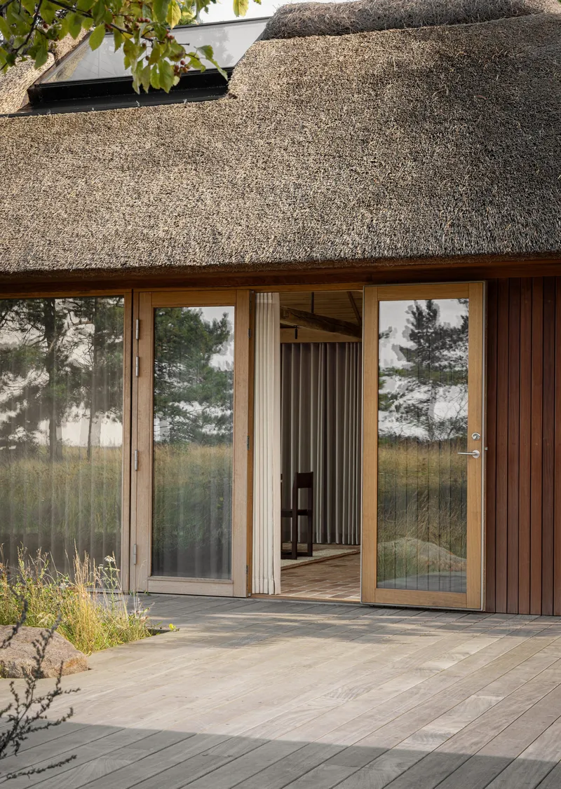 Thatched roof over sliding glass doors with vertical timber cladding and a wooden deck terrace