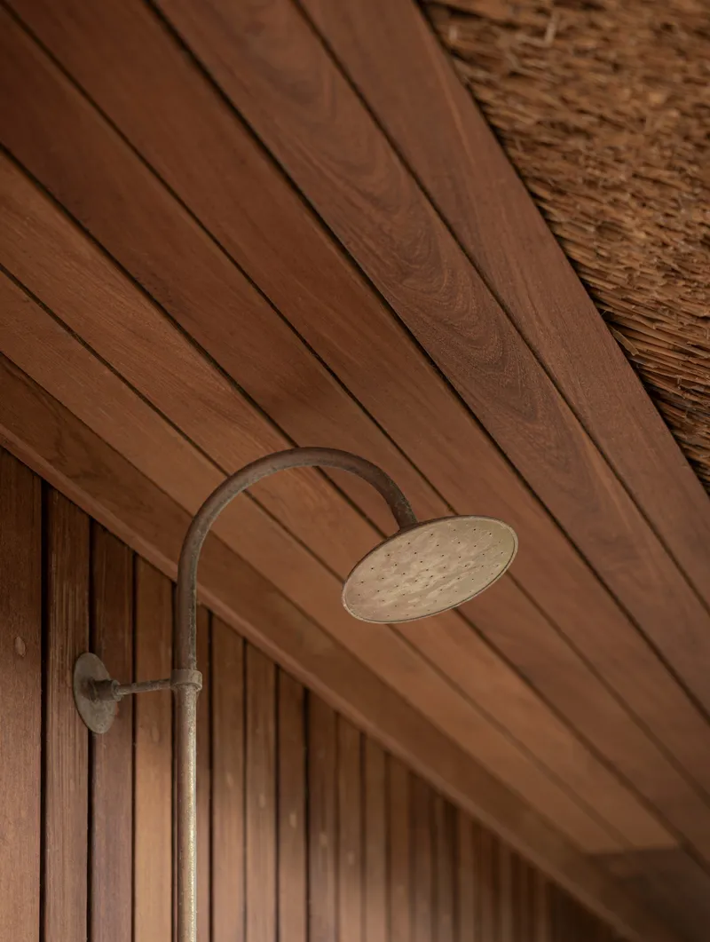 Exterior shower fixture mounted beneath a timber-planked soffit adjacent to thatched roofing
