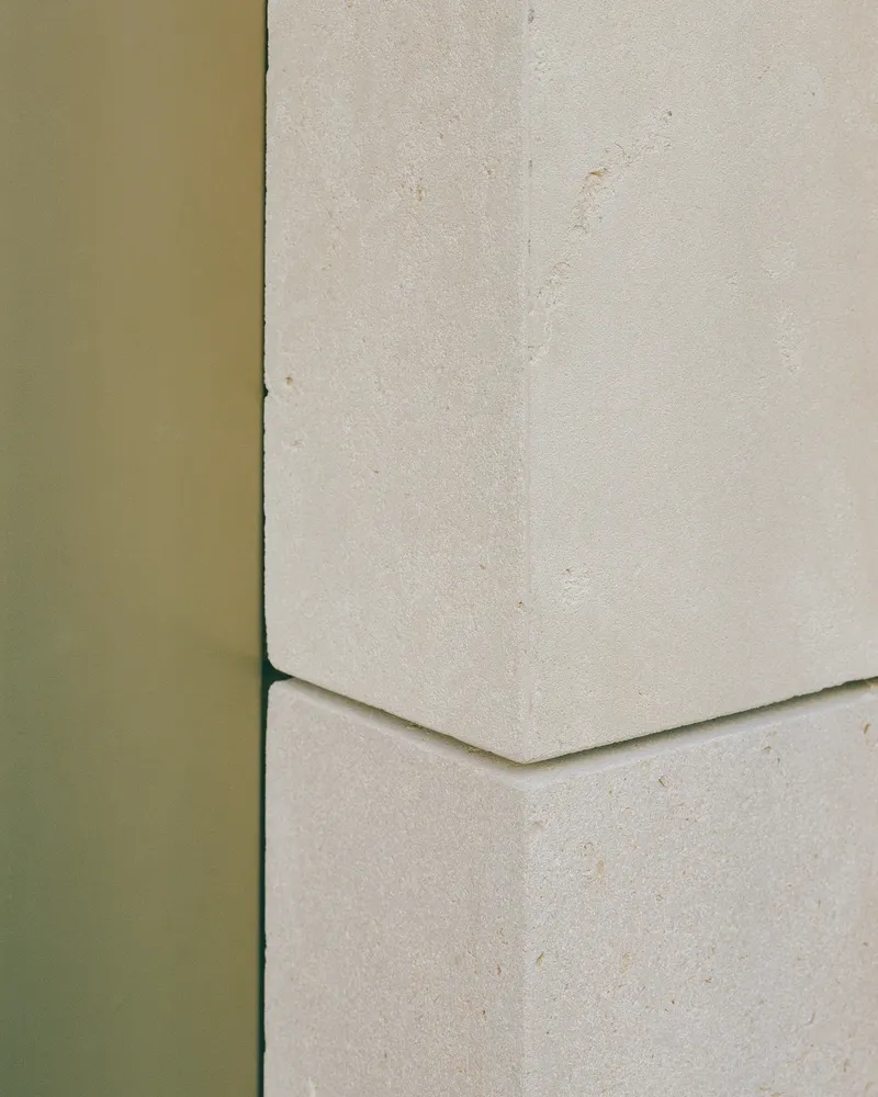 Detail of olive green metal edge meeting a pale stone panel with a chamfered joint