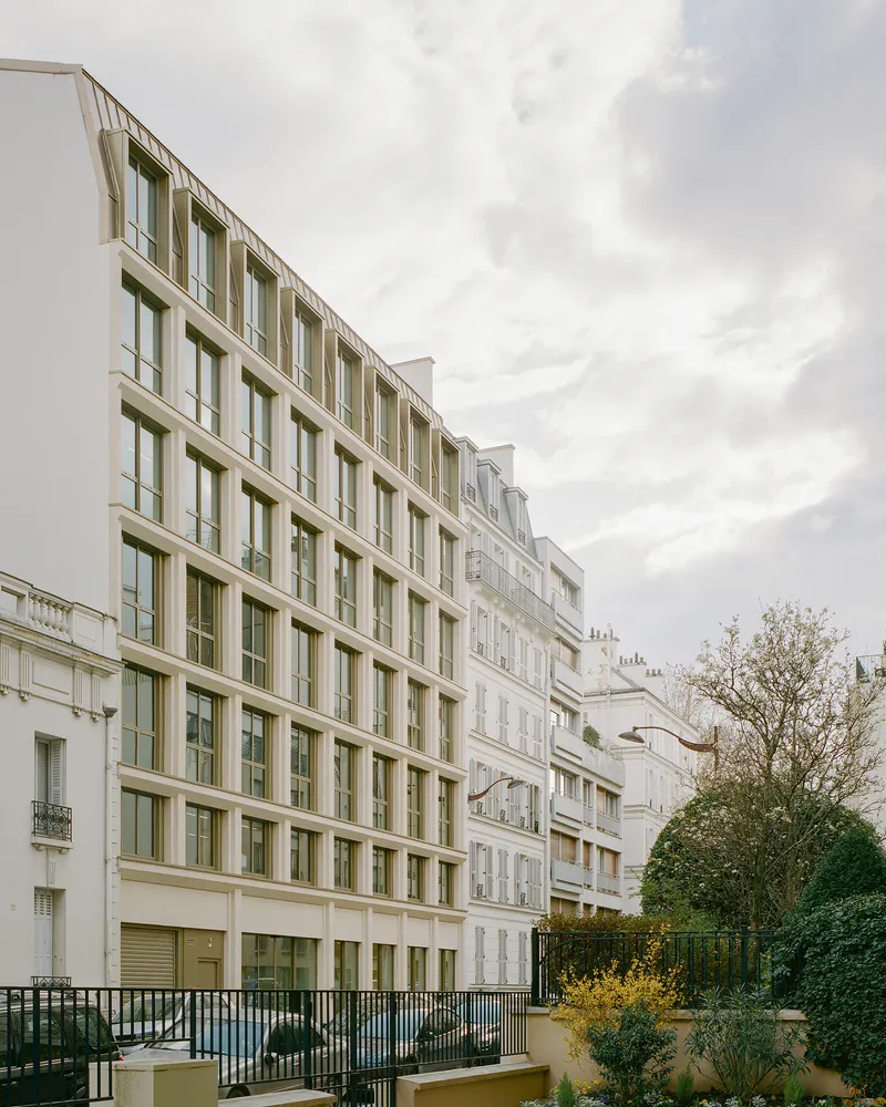 Street facade with recessed window grid under an overcast sky beside planted terraces and bare trees
