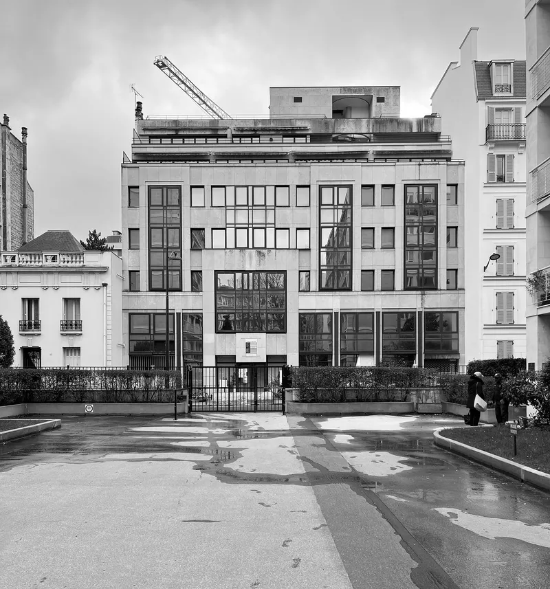 Street view of a five-story facade with rhythmic windows and a construction crane on the rooftop