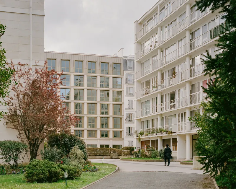 Courtyard view of the window grid facade with a figure walking the curved path in autumn