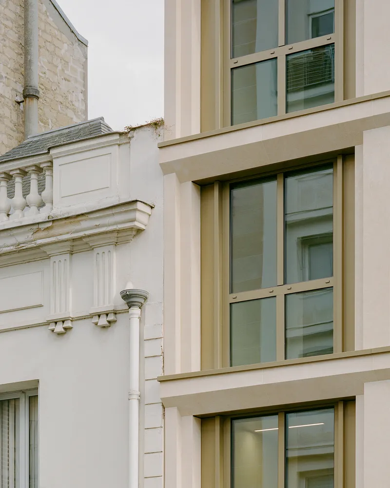 Close-up of the beige stone window frames meeting the white pilaster detail of an adjacent facade