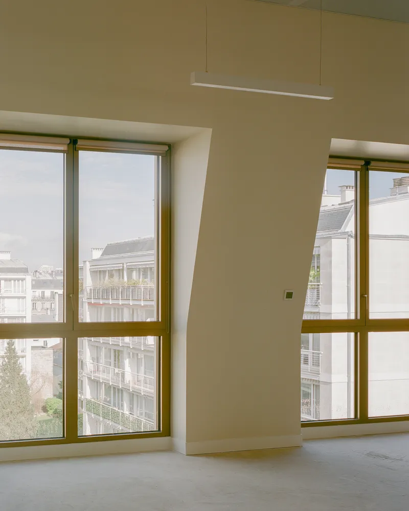 Interior corner with floor-to-ceiling windows framed in bronze metal and a suspended linear light fixture