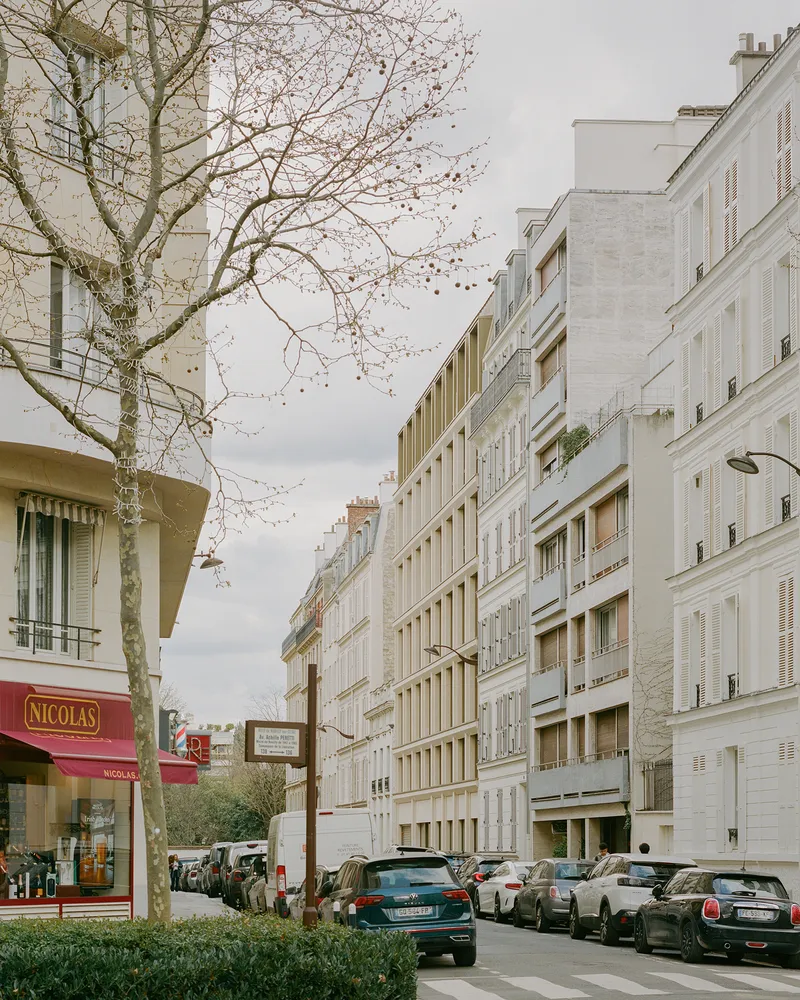 Street view of the white facade with horizontal shutters framed by bare winter trees and parked cars