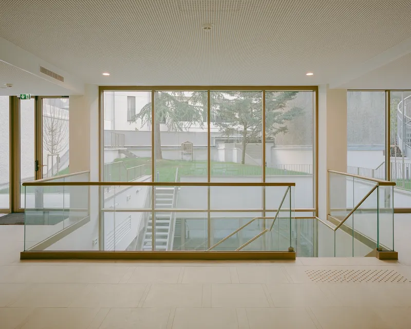 Glass and brass balustrade overlooking a courtyard garden with bare trees through floor-to-ceiling windows