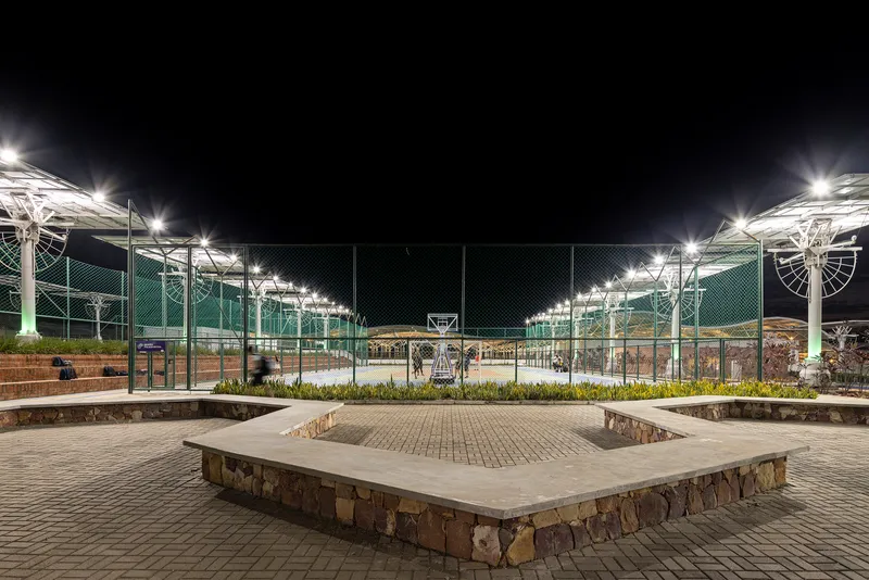 Stone and concrete seating platform with metal fencing and lit solar canopies beyond at night
