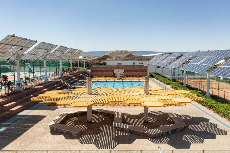 Yellow timber canopy structure casting geometric shadows over amphitheater seating and pool area