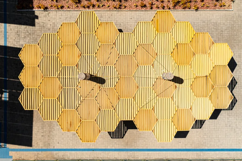 Overhead view of hexagonal yellow canopy modules suspended above open courtyard space
