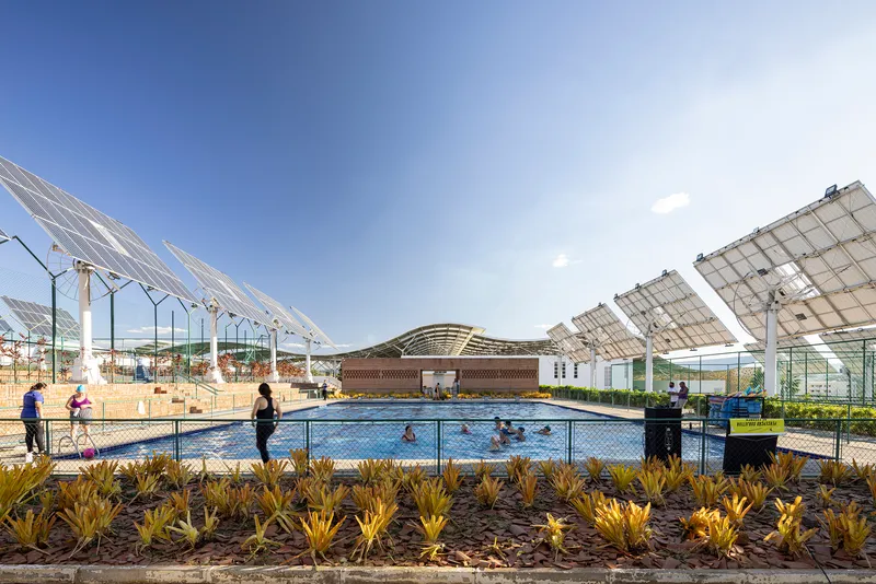 Outdoor swimming pool with fenced perimeter and overhead solar panel array under clear blue sky