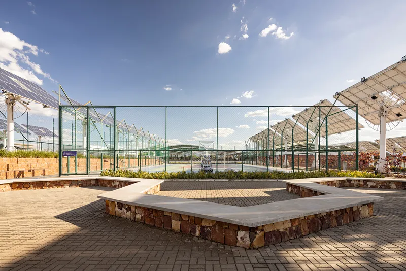 Concrete-topped stone bench in paved courtyard with glass-fenced sports court and solar canopy beyond