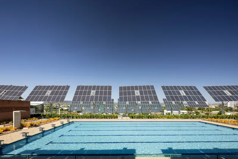 Swimming pool with lane markers beneath array of tilted solar panels and planted beds