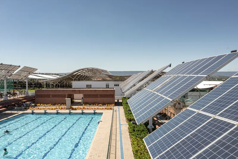 Outdoor lap pool flanked by tilted solar panel arrays and terraced seating under clear sky