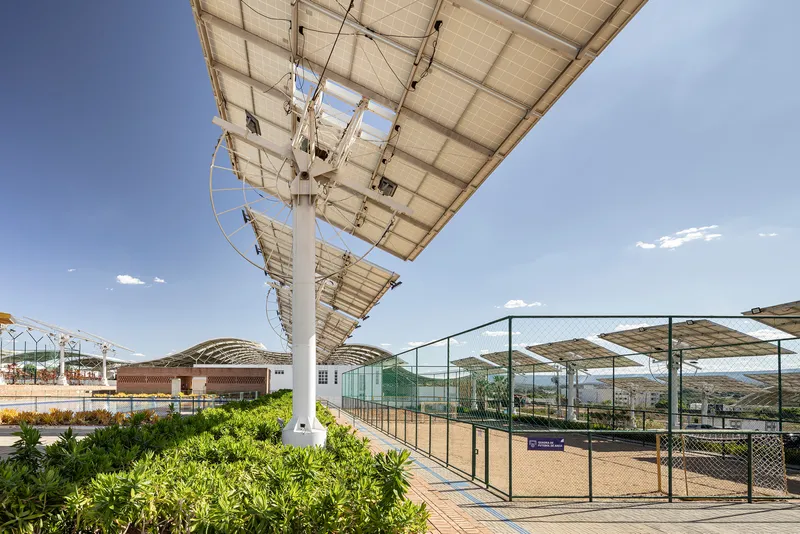 Sports court enclosed by chain-link fencing beneath angled solar canopy structures with distant hills