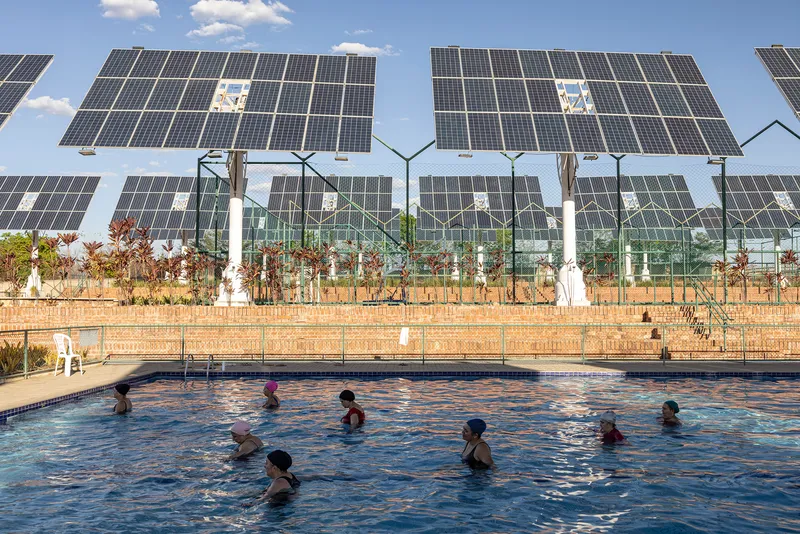 Swimming pool with children in the water backed by tracking solar panels and glass enclosure