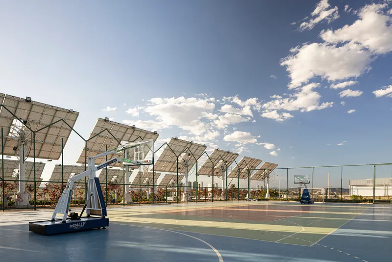 Basketball court with hoop and tilted solar panel canopy under partly cloudy afternoon sky