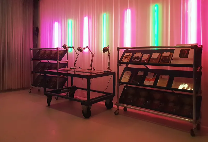 Wheeled display carts with task lamps arranged in a room with vertical neon light tubes