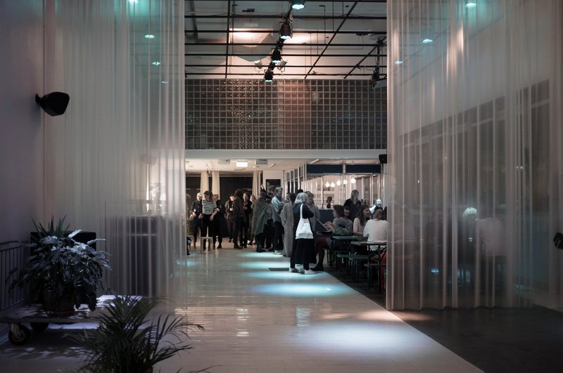 Translucent curtain partitions dividing the interior hall with people gathered in the illuminated spaces beyond