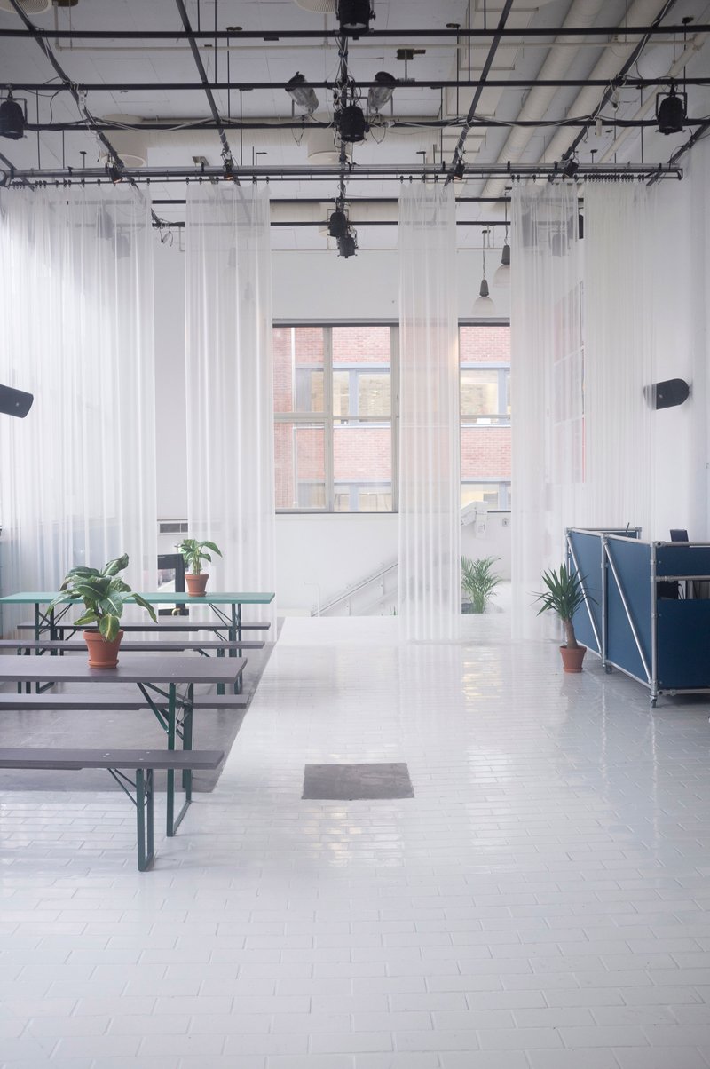 Folding bench tables on white tile flooring beneath windows overlooking adjacent brick buildings