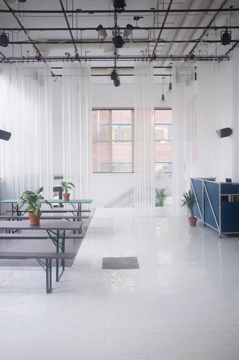 Folding bench tables on white tile flooring beneath windows overlooking adjacent brick buildings