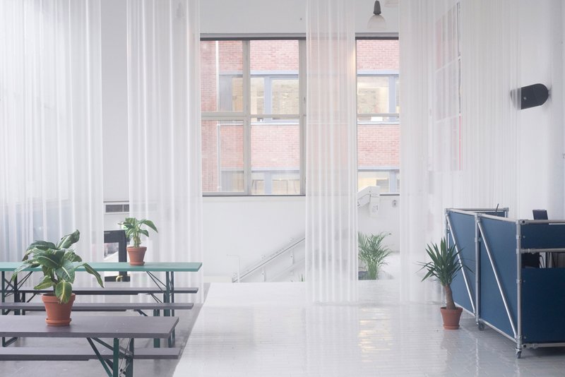 Interior view through sheer curtains with terracotta planters framing the simple furniture and window openings