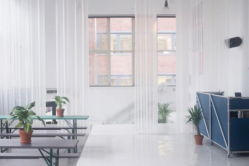 Interior view through sheer curtains with terracotta planters framing the simple furniture and window openings