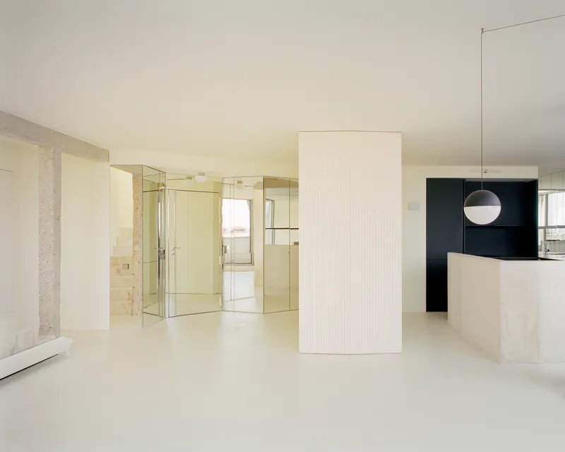 Open plan living area with fluted white volume, mirrored partition and black kitchen beyond