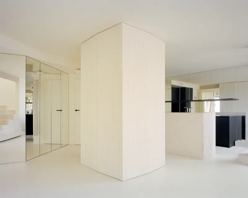 Freestanding fluted enclosure anchoring the space between mirrored doors and kitchen island