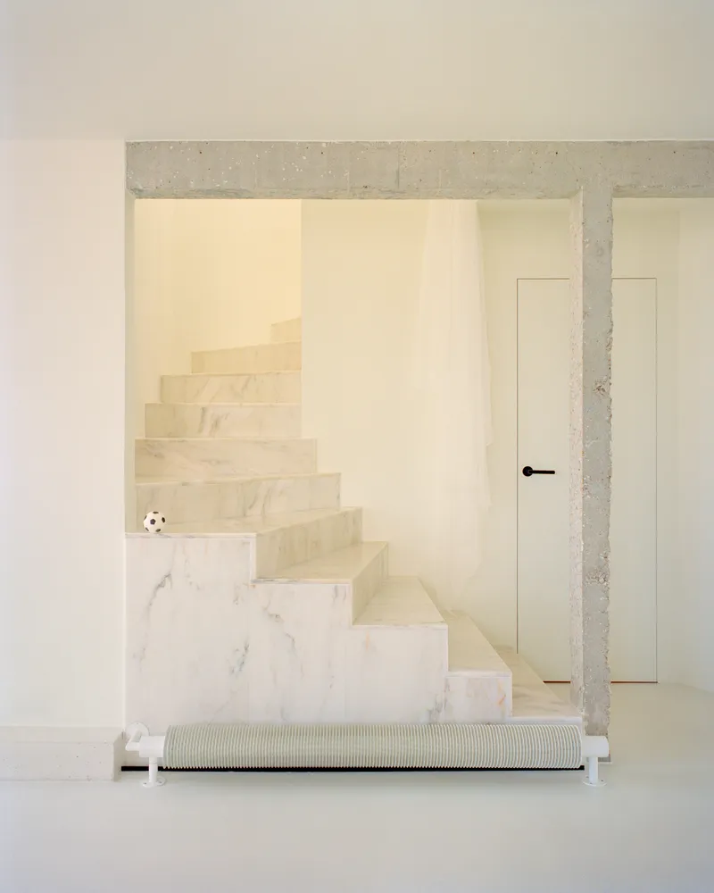 Marble staircase framed by exposed concrete lintel with white baseboard heater below