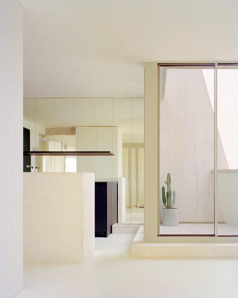 View through the kitchen island toward a glazed courtyard with a potted cactus in soft daylight