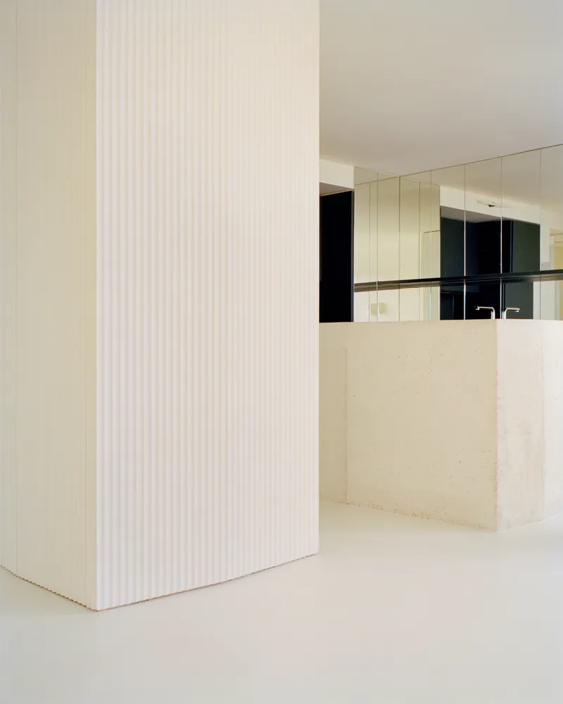 Fluted white column beside the pale stone kitchen island and mirrored upper cabinetry