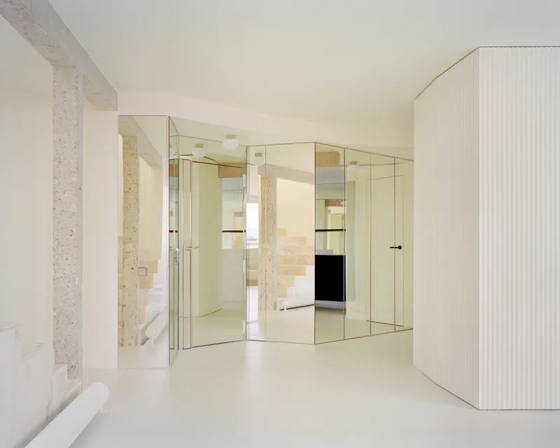 Mirrored glass partition wall reflecting the terrazzo columns and pale resin flooring