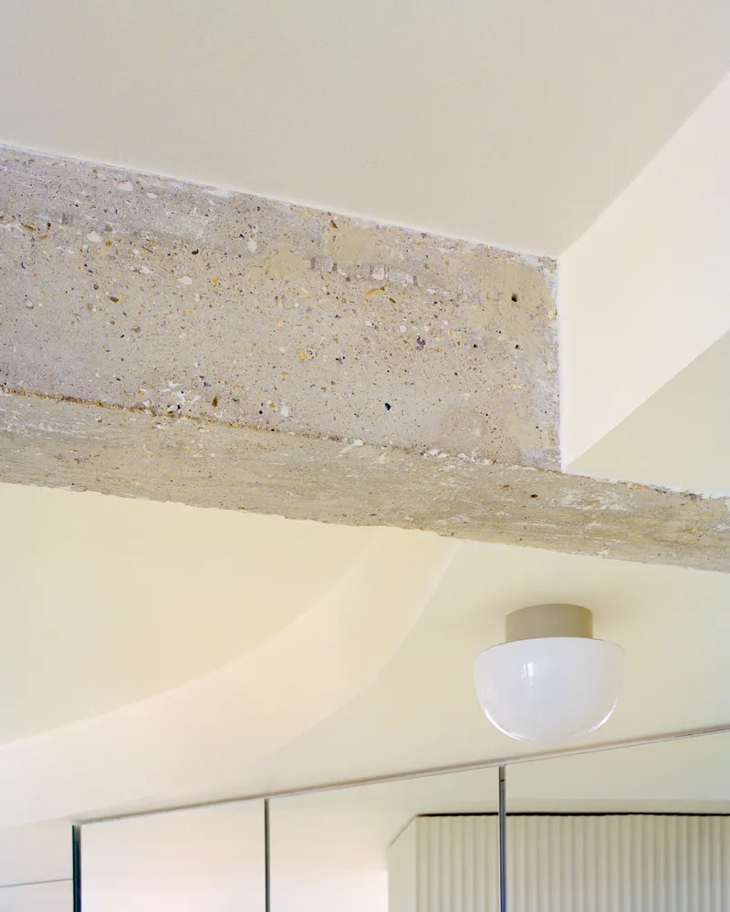 Exposed terrazzo beam spanning above a flush ceiling light and mirrored partition below
