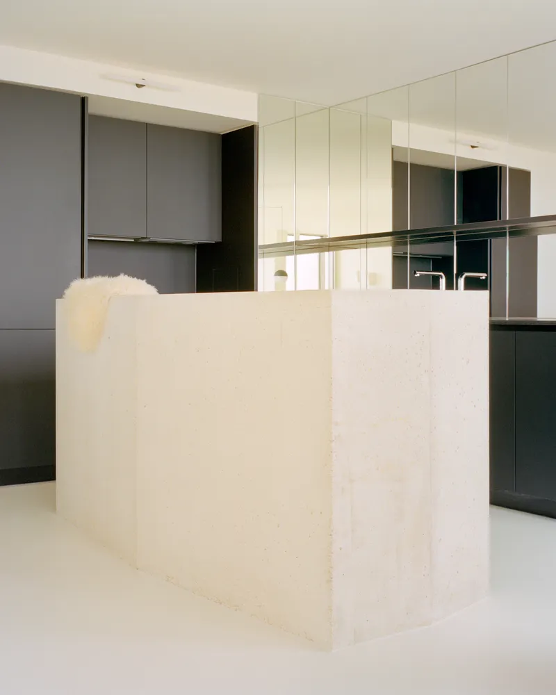 Pale limestone kitchen island with grey cabinetry and mirrored backsplash in bright daylight