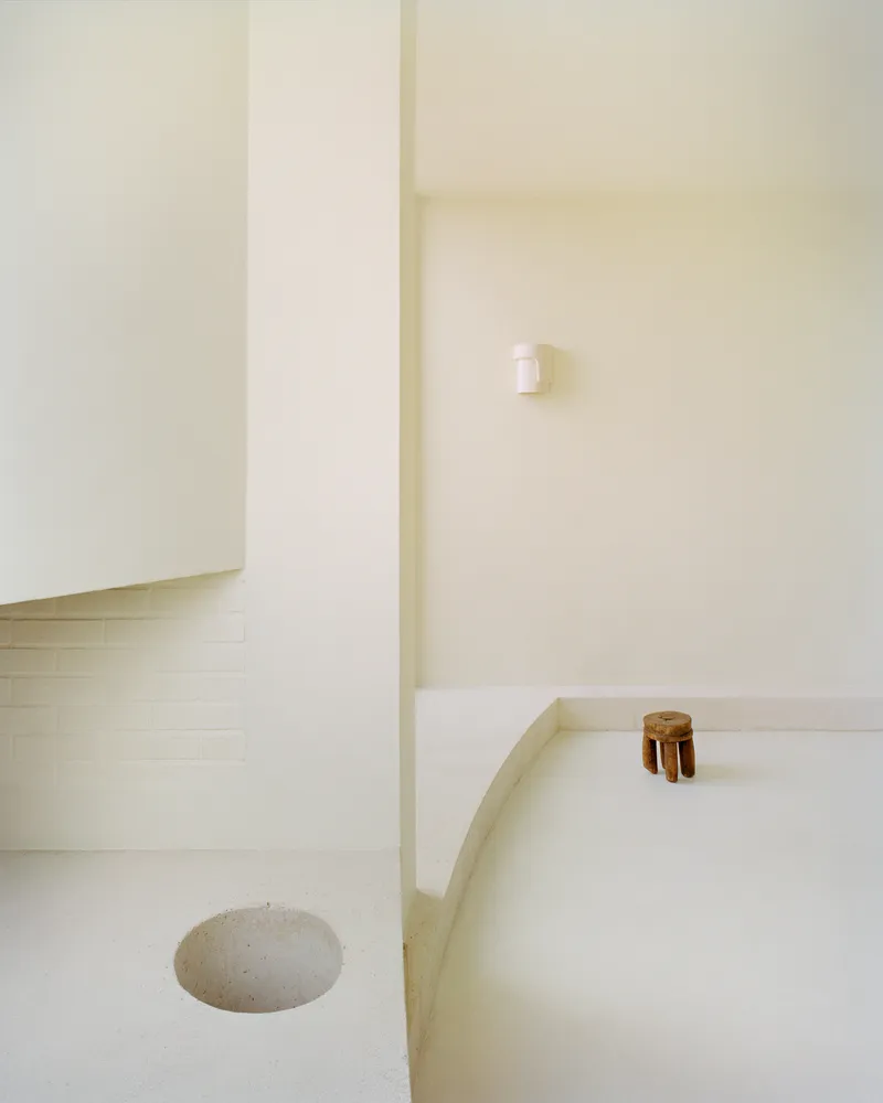 Sunken bath with pale tile surround and wooden stool beside a recessed floor drain