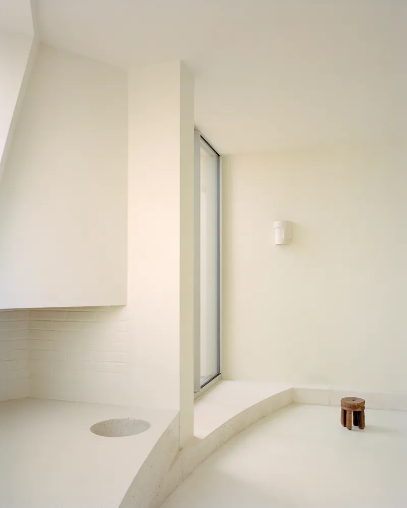 Sunken bathing area with sloped walls and a tall vertical window casting soft light