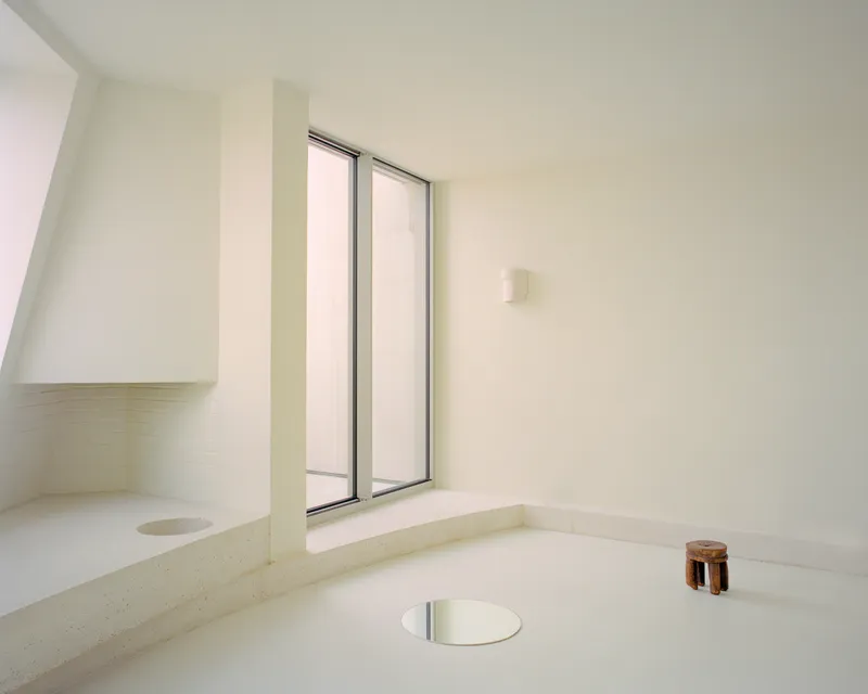 Sunken bath with wide double window and circular floor drain under diffused daylight