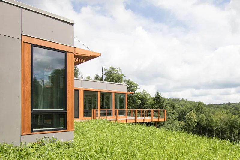 Corner detail showing timber-framed glazing and railing on a grassy slope in summer