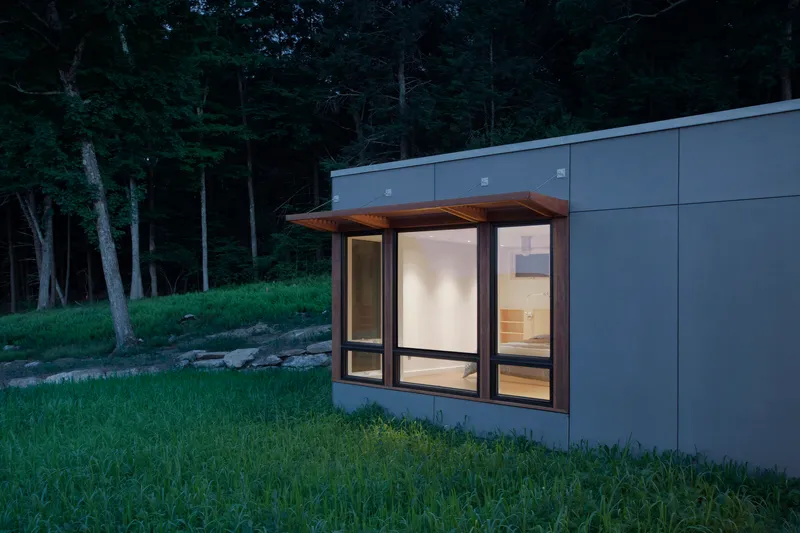 Corner bay window with timber soffit protruding from grey panel wall near wooded slope