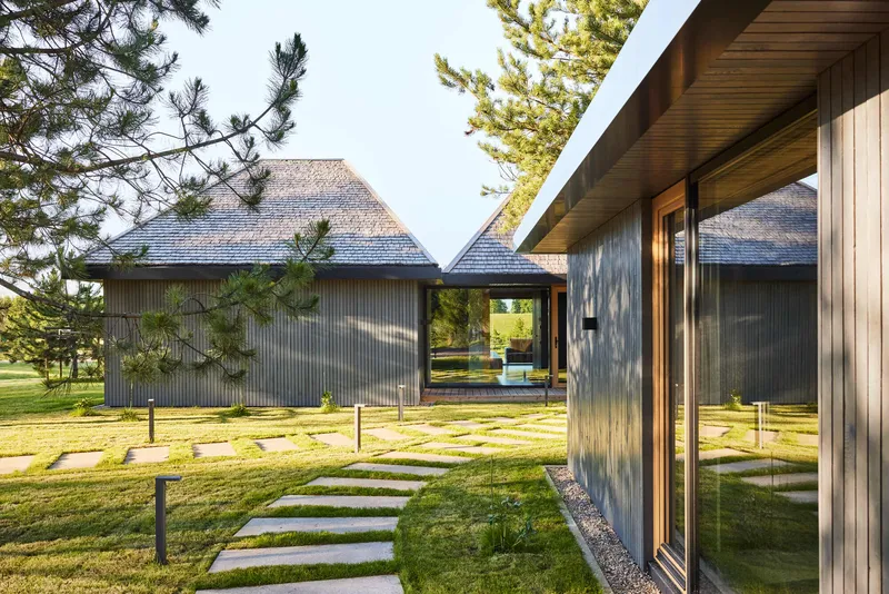 Courtyard view showing timber-clad volumes with pyramidal roofs connected by covered walkways and stepping stone paths