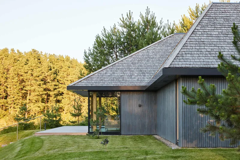Vertical timber cladding and pyramidal shingled roof with a covered terrace overlooking pines in afternoon light