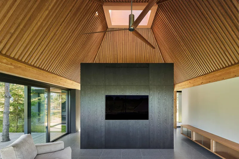 Living space with pyramidal timber slat ceiling, skylight, dark paneled fireplace core and ceiling fan