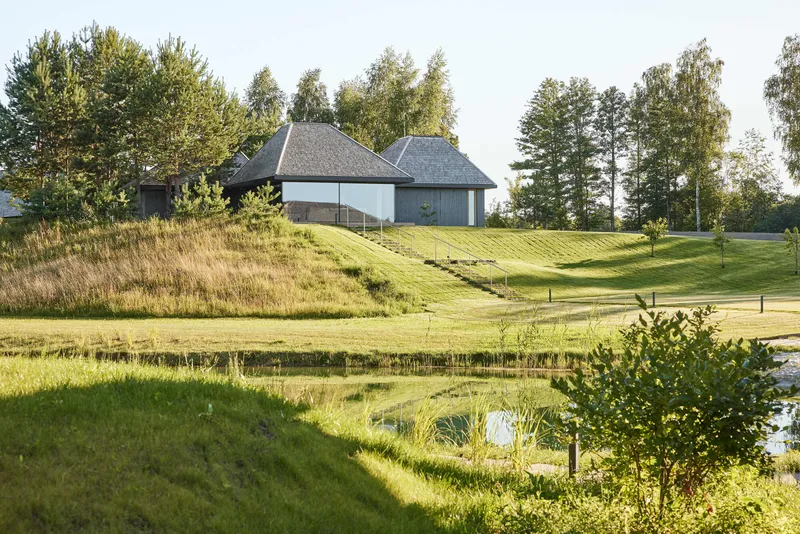 Cluster of conical roofs set on a terraced lawn above a pond with grasses and trees