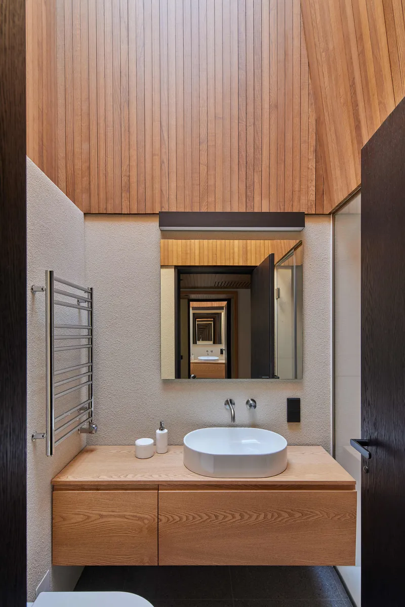 Bathroom vanity with timber ceiling and white basin beneath a mirror reflecting a doorway beyond