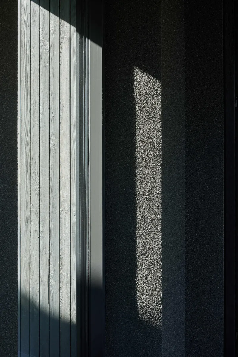Sunlight casting sharp shadows on dark textured wall beside white vertical timber cladding