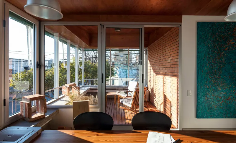 Interior dining space with timber ceiling and glazed doors opening to timber deck terrace with planted boxes