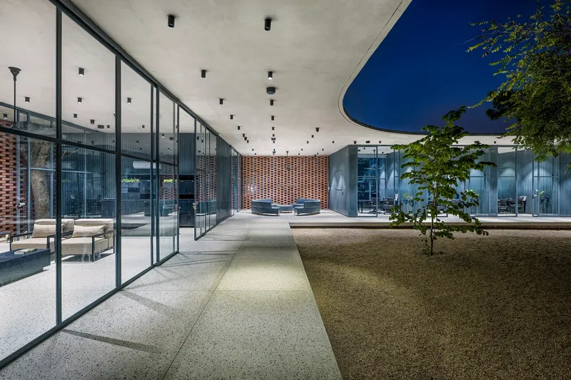 Central courtyard at dusk with gravel paths converging beneath a concrete roof and perforated brick screen wall
