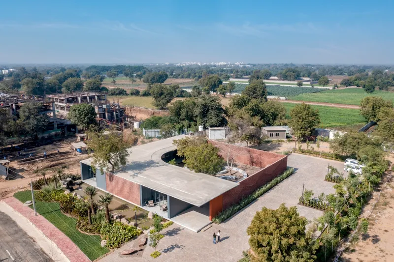 Aerial view of the low-slung concrete roof with perforated brick volume set among agricultural fields and trees